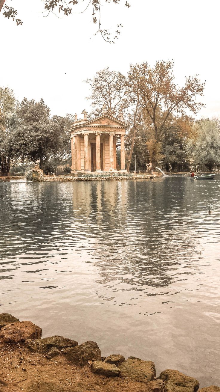 an old building sitting on top of a lake next to a forest filled with trees