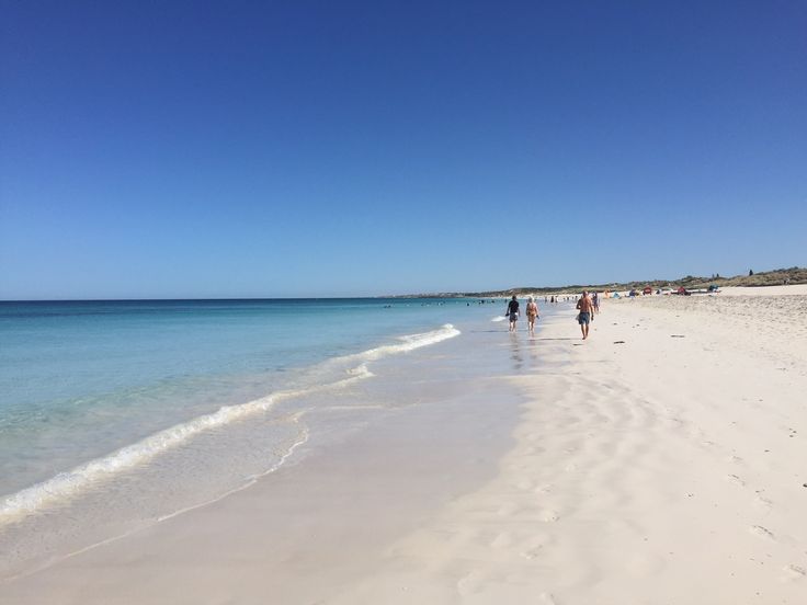 people are walking along the beach on a sunny day with clear blue water and white sand