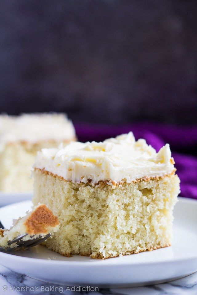 a slice of white cake on a plate with a fork and purple cloth in the background