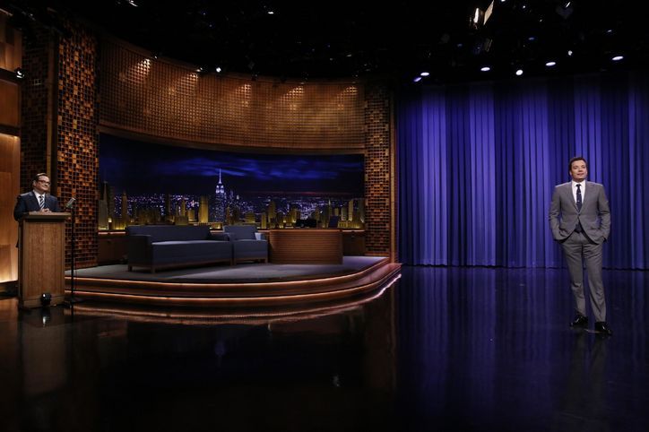 a man in a suit and tie standing next to a couch on a tv set