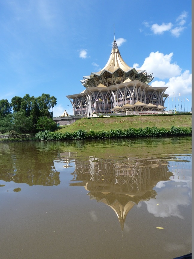 a large building sitting on top of a lush green field next to a river filled with water