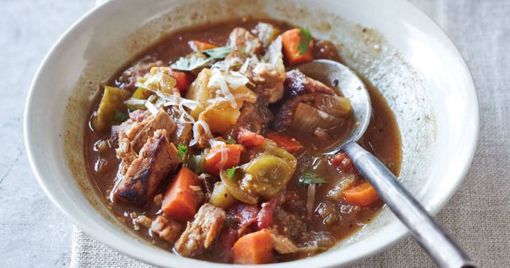 a white bowl filled with meat and vegetable stew on top of a cloth covered table