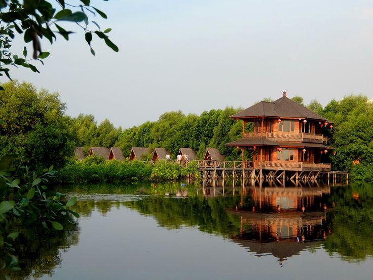 a wooden house sitting on top of a lake next to lush green trees in the background