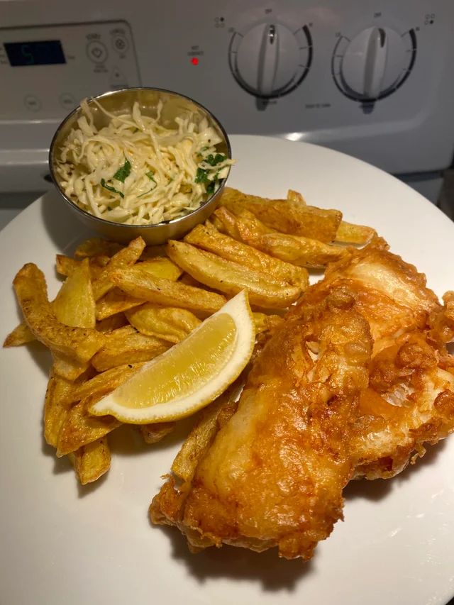 fish and fries on a plate with coleslaw, lemon wedges and grated parmesan cheese