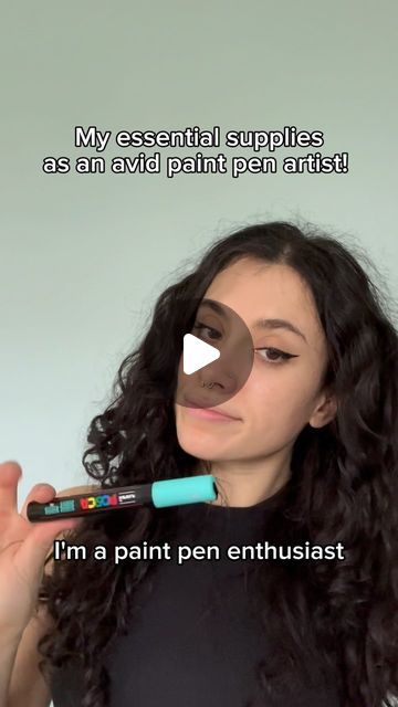 a woman holding a pen in her right hand with the caption, my essential supplies as an avid paint pen artist