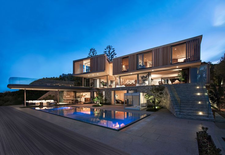 a large house with a swimming pool in front of it at night, surrounded by greenery