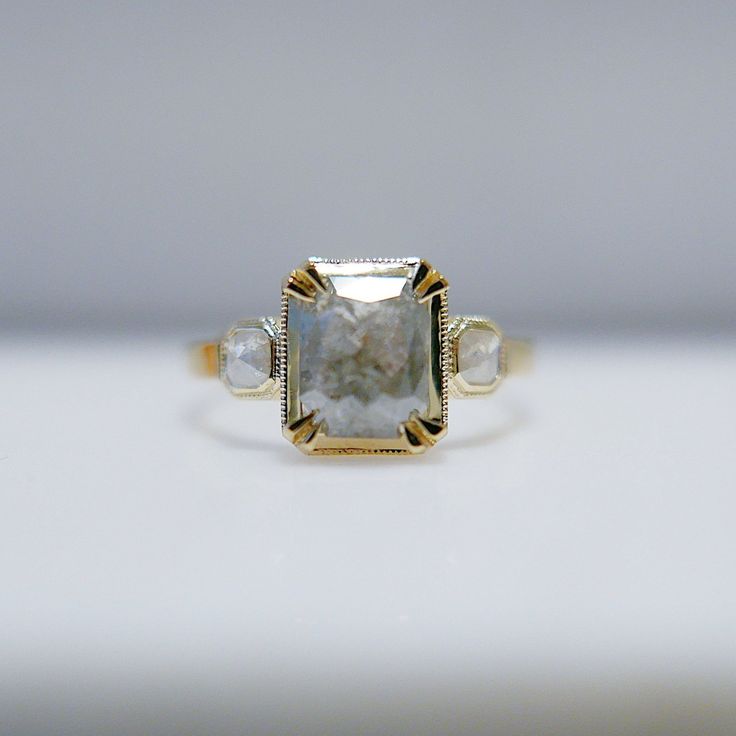 a yellow gold and white diamond ring with three stones on the sides, sitting on a table