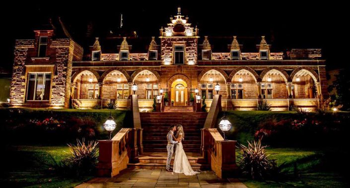 a bride and groom standing in front of a large building at night with lights on