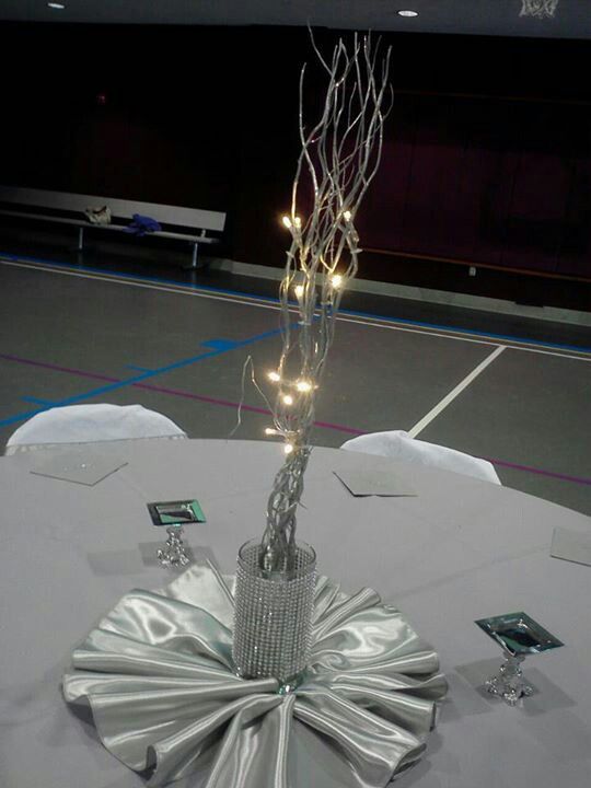 a table topped with a silver cloth covered tablecloth and a vase filled with lights