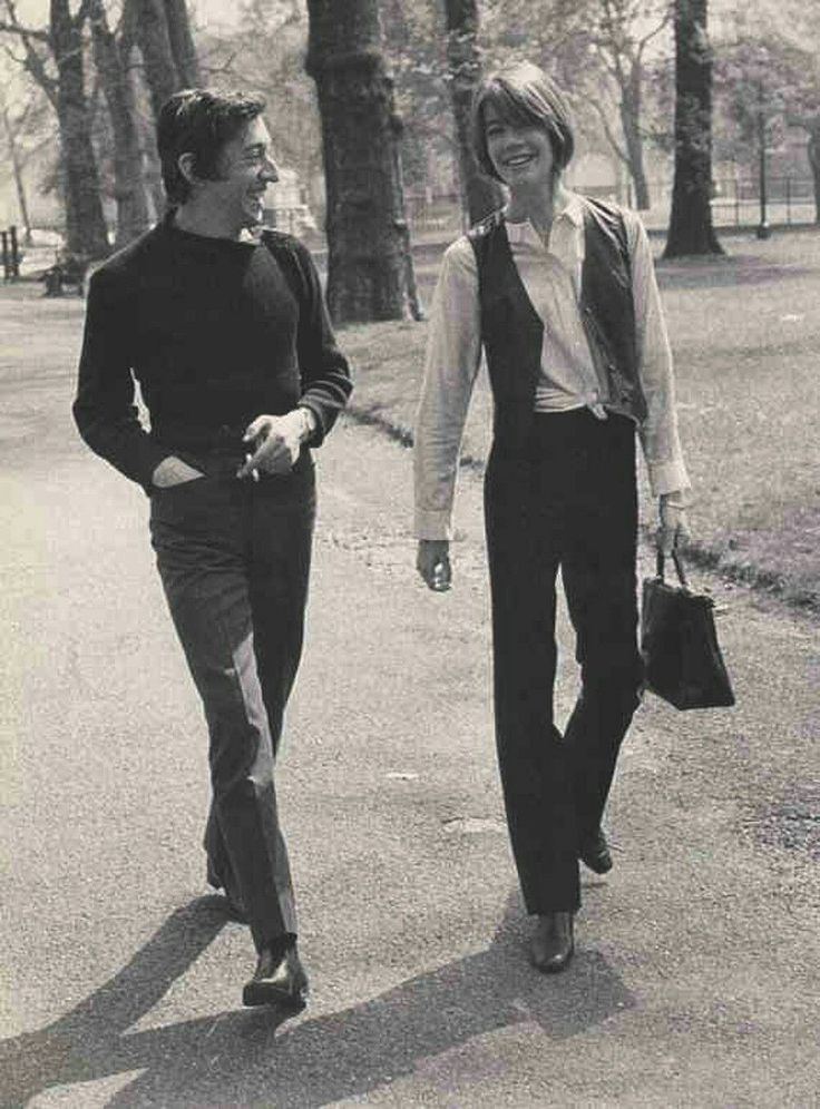 a man and woman walking down the street in black and white, with trees in the background