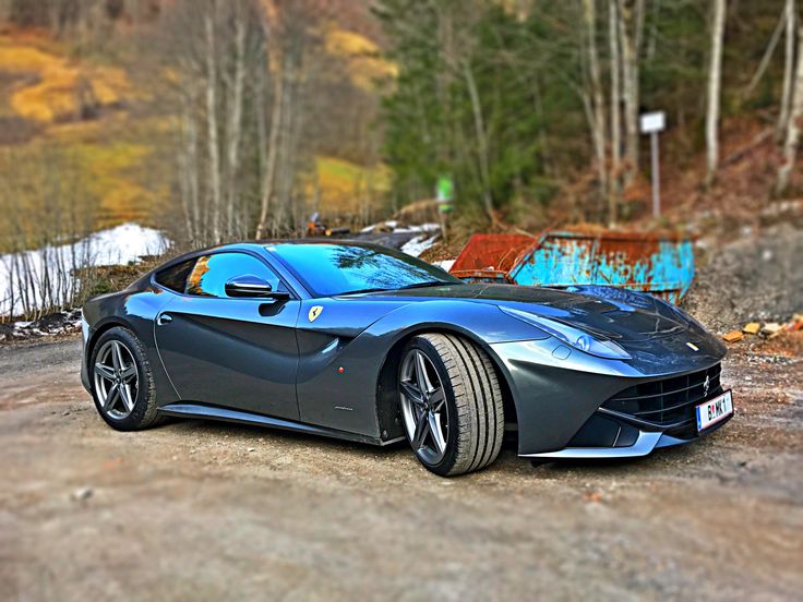 a blue sports car parked on the side of a dirt road in front of trees