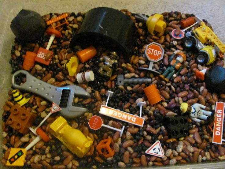 a plastic container filled with lots of different types of toy cars and construction vehicles on top of gravel