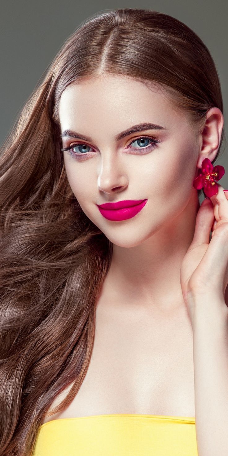 a woman with long brown hair and bright pink lipstick holding a flower in her hand