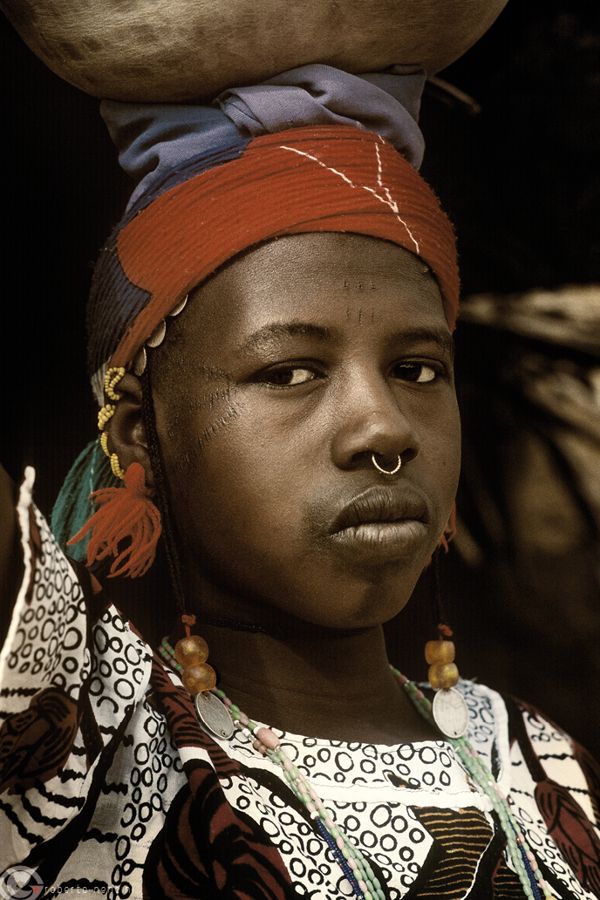 a woman with a large bowl on her head and an orange nose ring around her neck