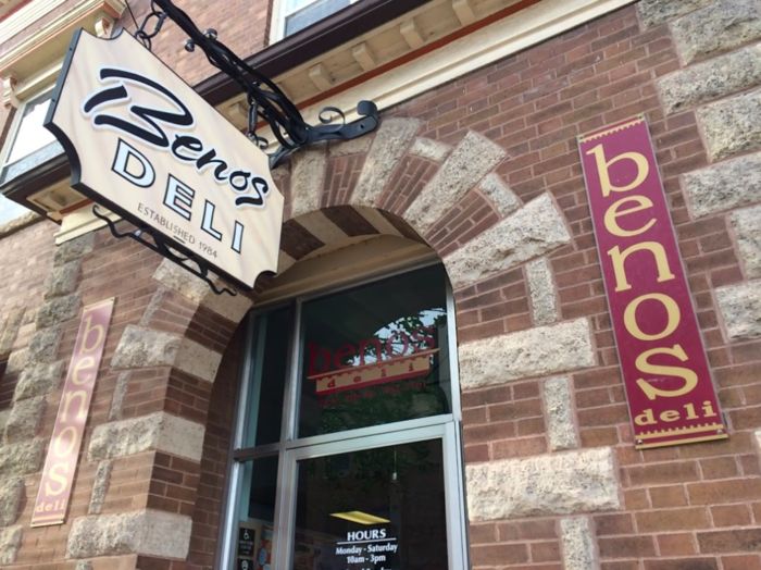 a restaurant sign hanging from the side of a brick building next to a window with an open door