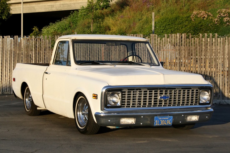 an old white pickup truck parked in a parking lot next to a wooden picket fence