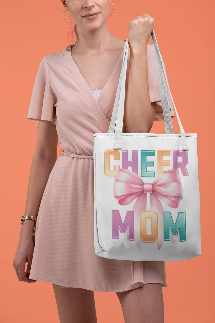 Elevate your game day essentials with our "Cheer Mom" 📣 Canvas Tote Bag! Perfect for proud cheerleader moms, this durable, eco-friendly tote showcases a vibrant, large pink bow 🎀 and colorful letters "Cheer Mom" print on both sides, embodying the spirit of cheerleading with style and convenience. Crafted to carry all your necessities, from pom-poms to snacks, its spacious interior and sturdy handles make it your go-to bag for every cheer event and beyond.  Available in 3 sizes to add both functionality and style, these custom-printed tote bags come with multiple handle colors to match your designs. Made with spun polyester, these bags feature double-stitched seams, cotton webbing straps, and nonwoven laminate lining for high-end durability.  .: Made with 100% polyester, a medium-weight f Casual Shoulder Bag For Mother's Day, Retro White Bags With Letter Print, Retro White Bag With Letter Print, White Canvas Shoulder Bag For Mother's Day, White Shoulder Bag With Letter Print For Mother's Day, Fun White Letter Print Bag, White Canvas Bag For School, Cheerleading Mom, Cheer Competition