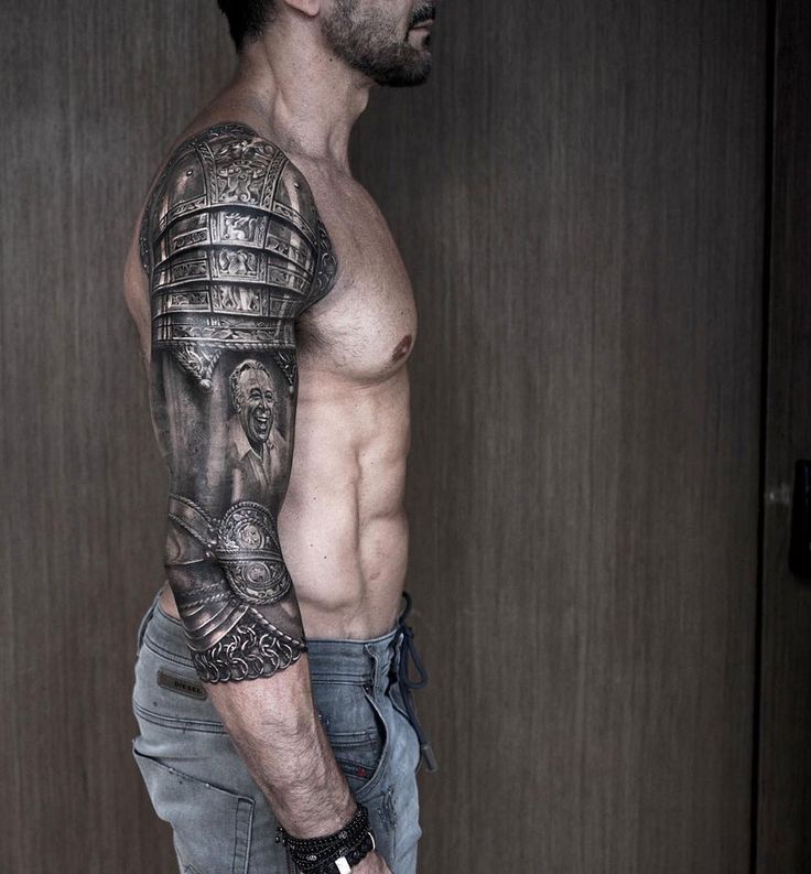 a man with a tattoo on his arm is standing in front of a door and wearing jeans