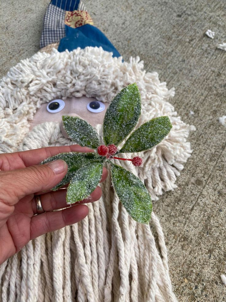 a person holding a fake leaf in front of a stuffed animal with green leaves on it's head