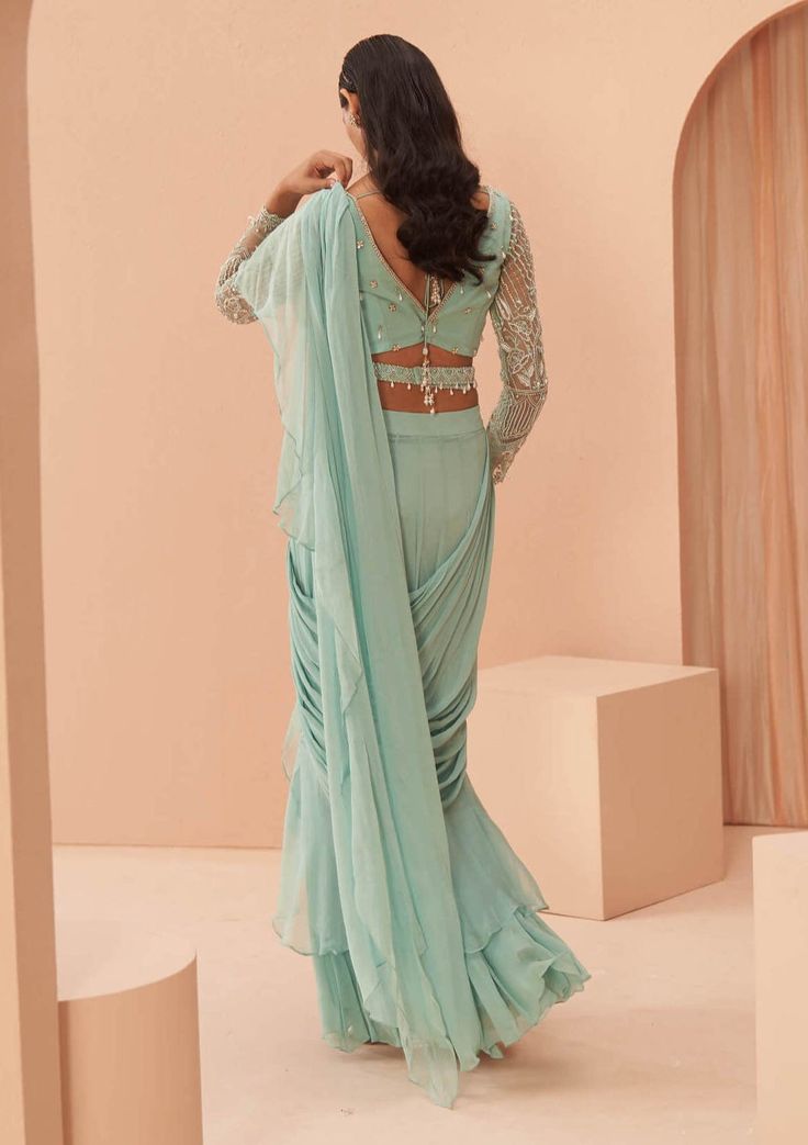 Editors Note Step into elegance with this delicate draped ruffle sari paired with an embroidered full sleeves blouse. This ensemble combines timeless charm with modern sophistication, making it a perfect choice for special occasions where you want to make a lasting impression. Elegant Pre-draped Fitted Saree With Ruffles, Georgette Sets With Draped Sleeves, Traditional Draped Sets With Ruffles, Green Georgette Saree With Ruffles, Elegant Pre-draped Ruffled Saree For Eid, Green Ruffled Saree For Wedding, Traditional Draped Ruffle Sharara, Elegant Draped Sharara With Cutdana, Traditional Draped Ruffles Sharara