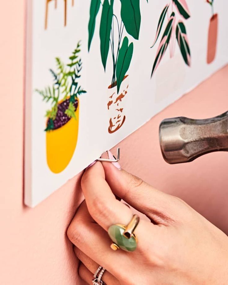 a woman's hand holding onto a wall with flowers and plants on it, next to a pair of scissors