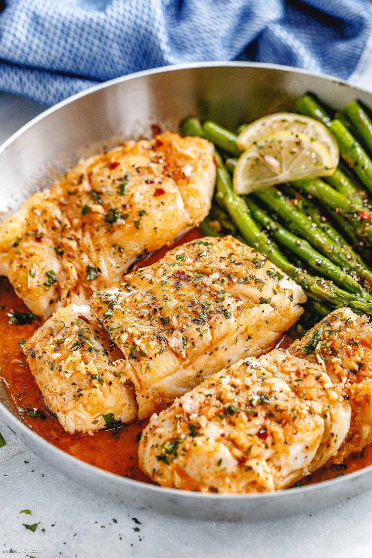 a pan filled with chicken, asparagus and lemon wedges on top of a table