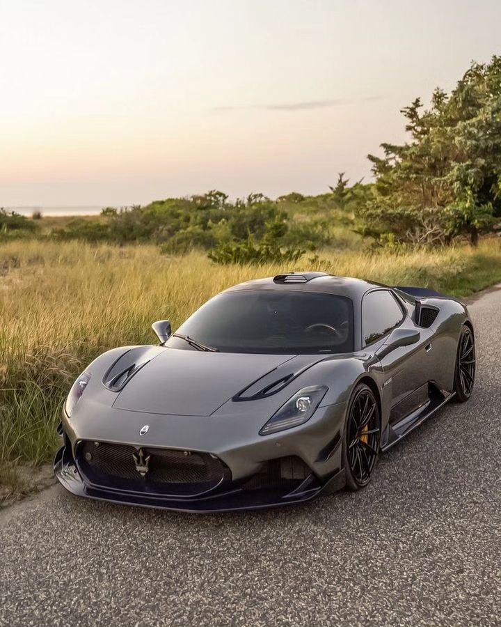 a grey sports car parked on the side of a road next to grass and trees