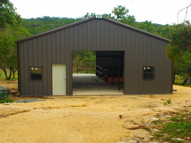 a garage with two doors open in the middle of a dirt lot next to trees