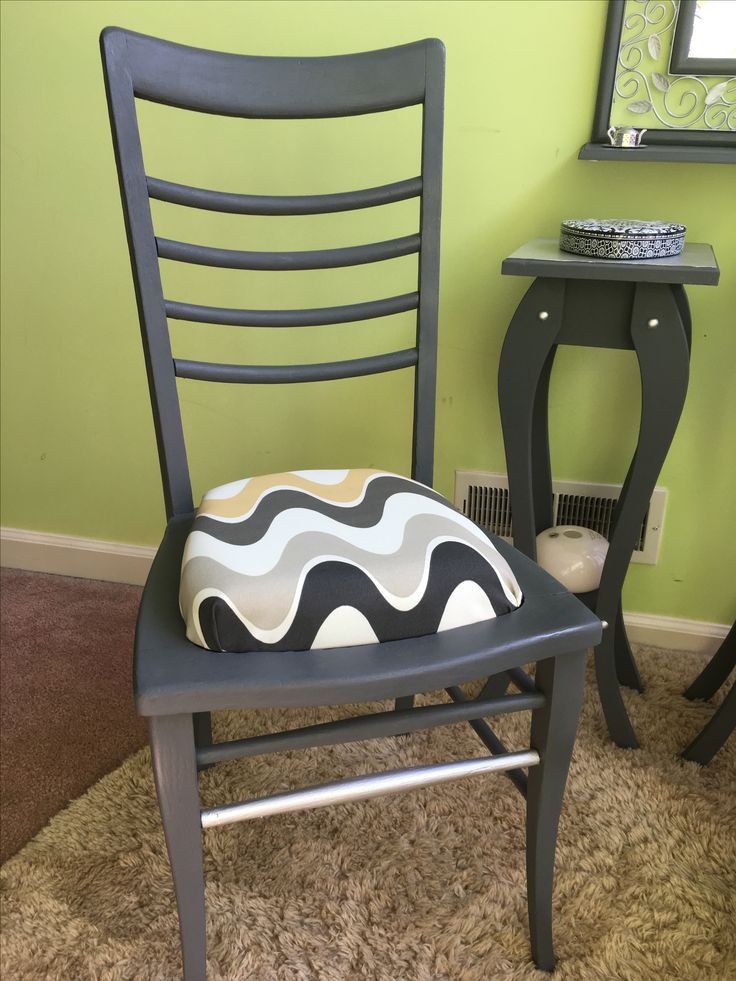 a chair with a cushion on it next to a small table and mirror in a room