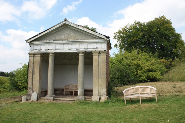 an old building sitting on top of a lush green field next to a white bench