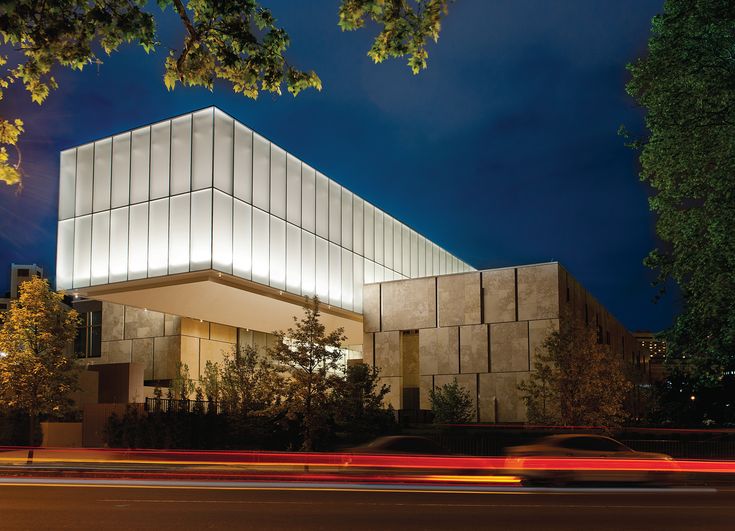 a building that is lit up at night with cars passing by in the foreground