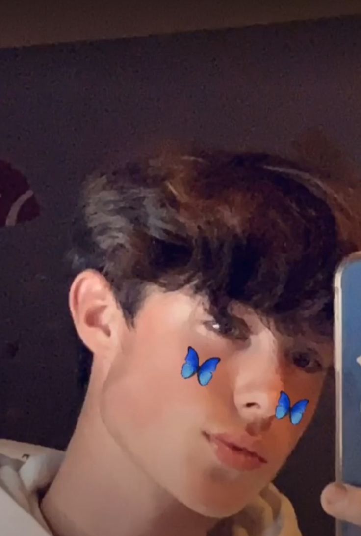 a young man holding up a cell phone with blue butterflies on his face