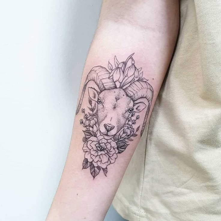 a woman's arm with a ram and flowers tattoo on the left side of her arm