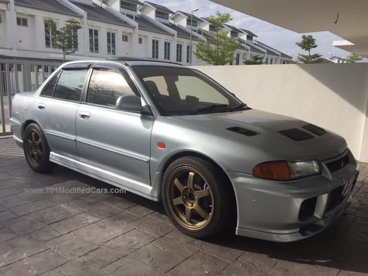 a silver car parked in front of a white wall and some buildings on the other side