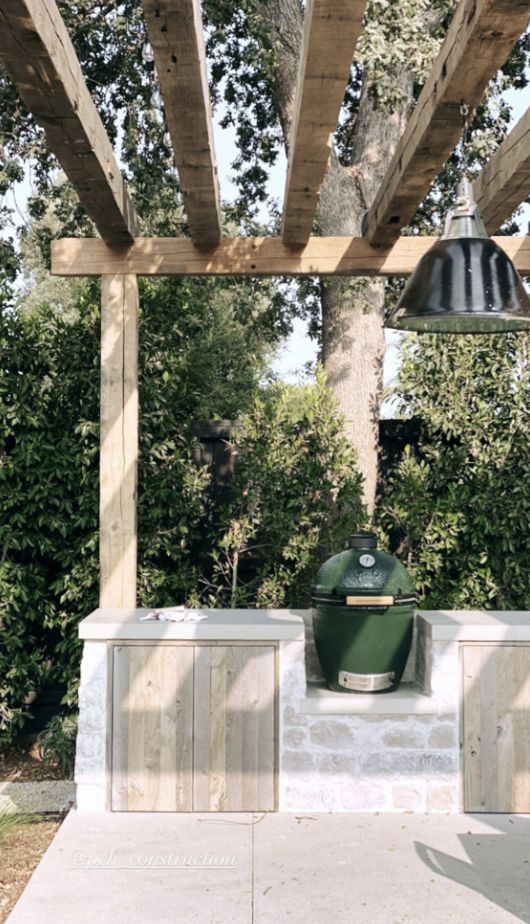 an outdoor bbq grill under a pergolated roof with two lights on it