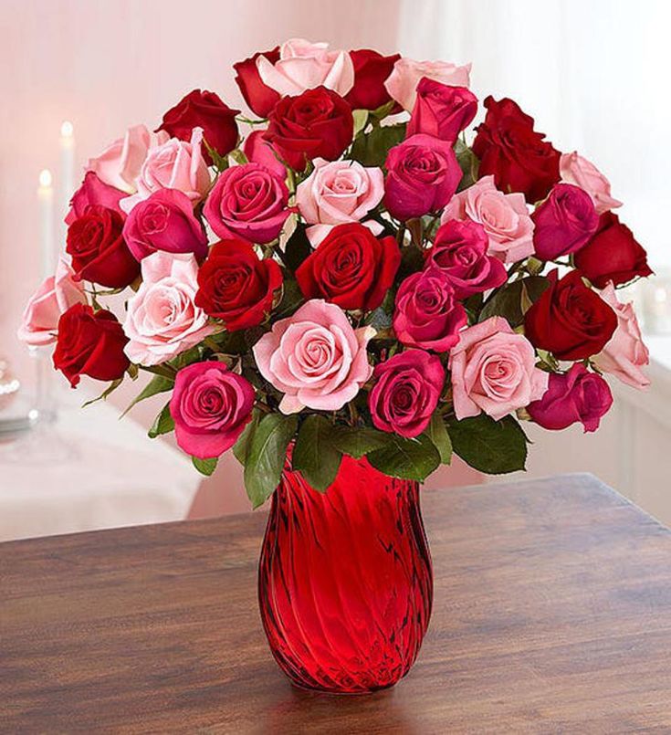 a red vase filled with lots of pink and red roses on top of a wooden table