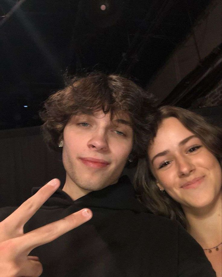 a young man and woman posing for the camera with their peace sign in ...