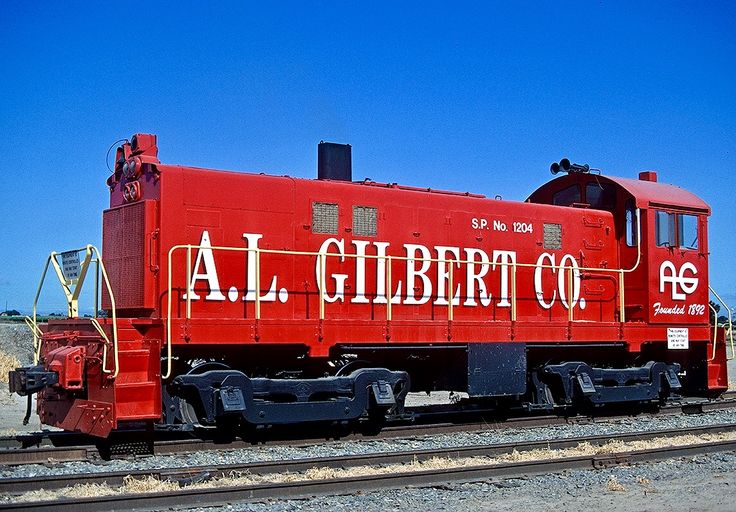 a red train engine with graffiti on it's side sitting on the tracks in front of a blue sky