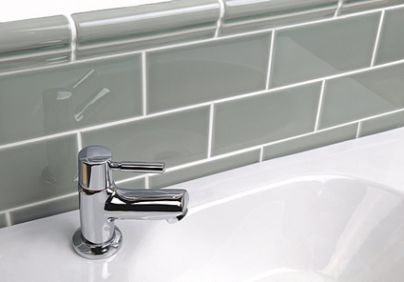 a white sink sitting under a faucet next to a green tile backsplash