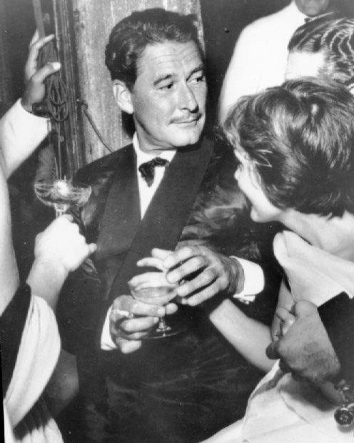 an old black and white photo of a man in a tuxedo talking to two women