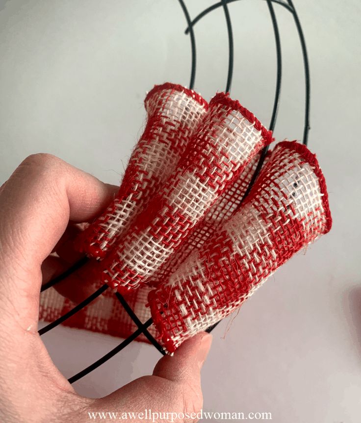 someone is holding some red and white fabric on a wire rack with scissors in it