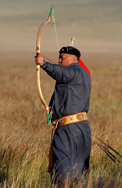 a man in uniform is holding a bow and arrow while standing in the tall grass