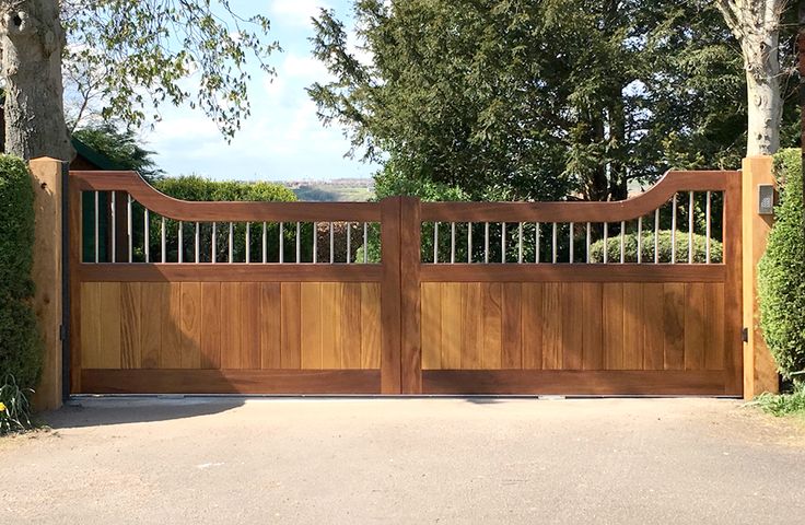 a large wooden gate in the middle of a driveway with trees and bushes around it