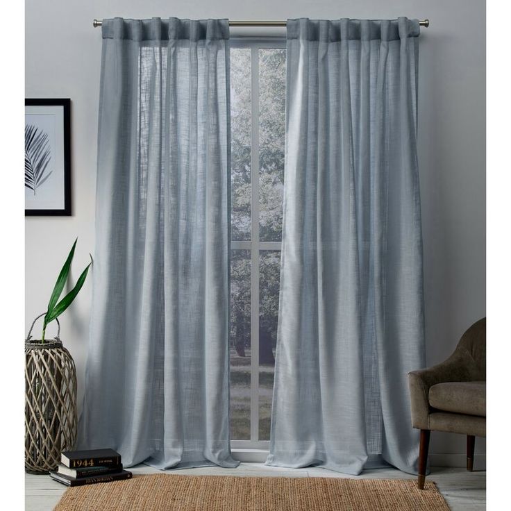 a living room with a large window covered in light blue curtains and a rug on the floor