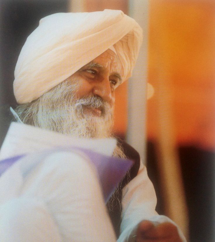 an old man wearing a white turban and holding something in his hand while looking at the camera