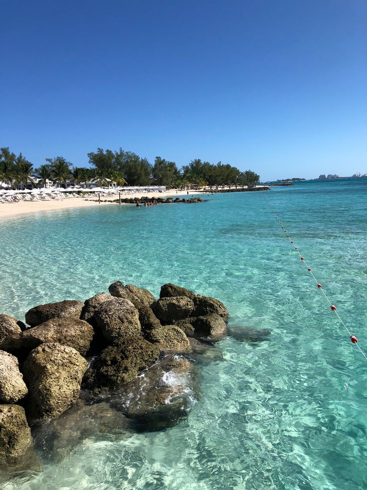 the water is crystal blue and clear with rocks in front of it, while people are swimming