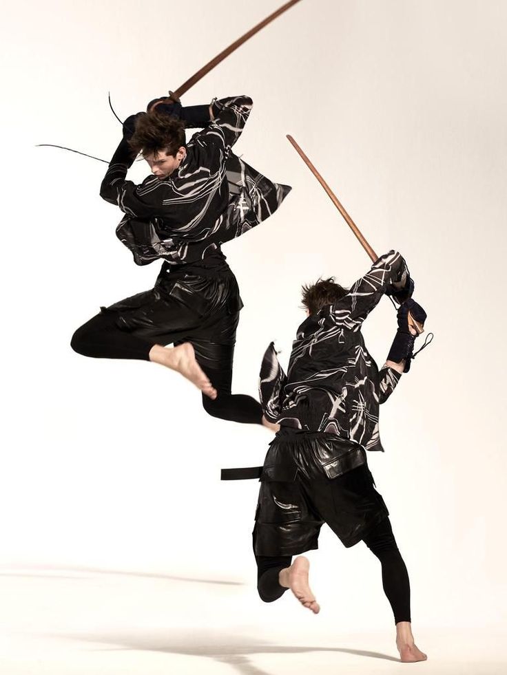 two people in black and white outfits are performing an acrobatic move with swords