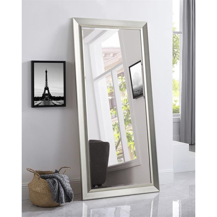 a large white mirror sitting on top of a floor next to a vase with flowers