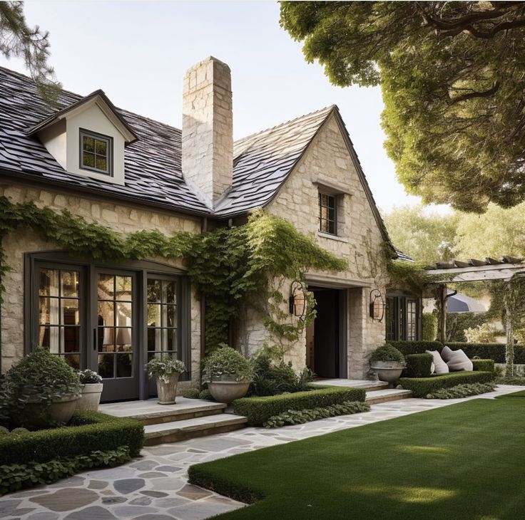 a stone house with lots of greenery on the front and side windows, surrounded by grass