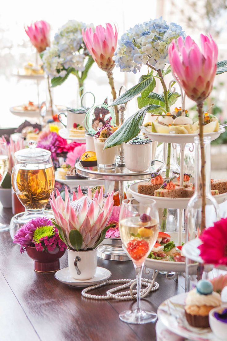 a wooden table topped with lots of plates and cups filled with food next to flowers